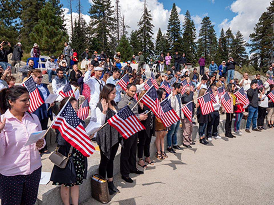 People at a naturalization ceremony saying the Oath of Allegiance and holding American Flags.