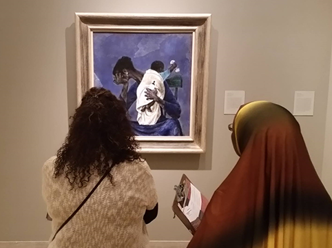Two women looking at a piece of art hanging on the wall of a mother holding her child.