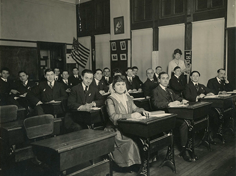 Historic photo of people sitting at desks in a large room.