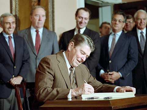 Picture of President Ronald Reagan signing a law with various officials looking on.