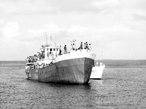 Image of a Mariel boatlift vessel, crowded with Cuban refugees, approaches Key West escorted by a U.S. ship in 1980. *USCIS History Library