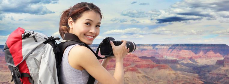 Woman with a backpack and a camera takes a picture of the Grand Canyon