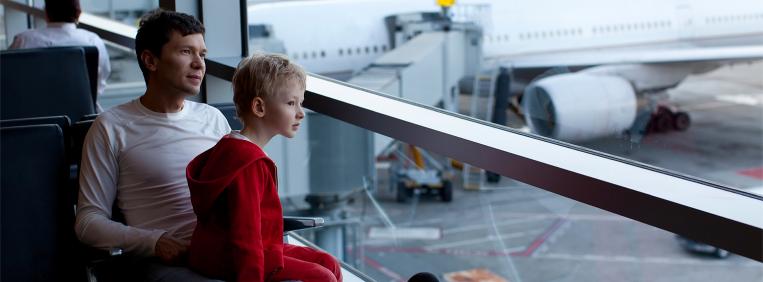 Man with young boy on his lap staring out the window at airplanes at an airport